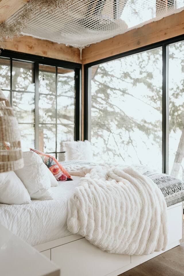 Cozy bedroom with a plush white-layered bed beneath floor-to-ceiling windows and an overhead hammock net.