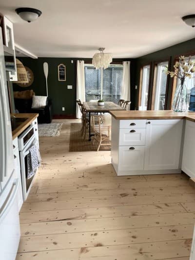 Open-plan kitchen with refinished pine floors leading to the dining table and leather couch living area.