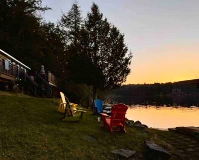 Colourful Adirondack chairs on the lawn facing a glowing sunset over the lake.