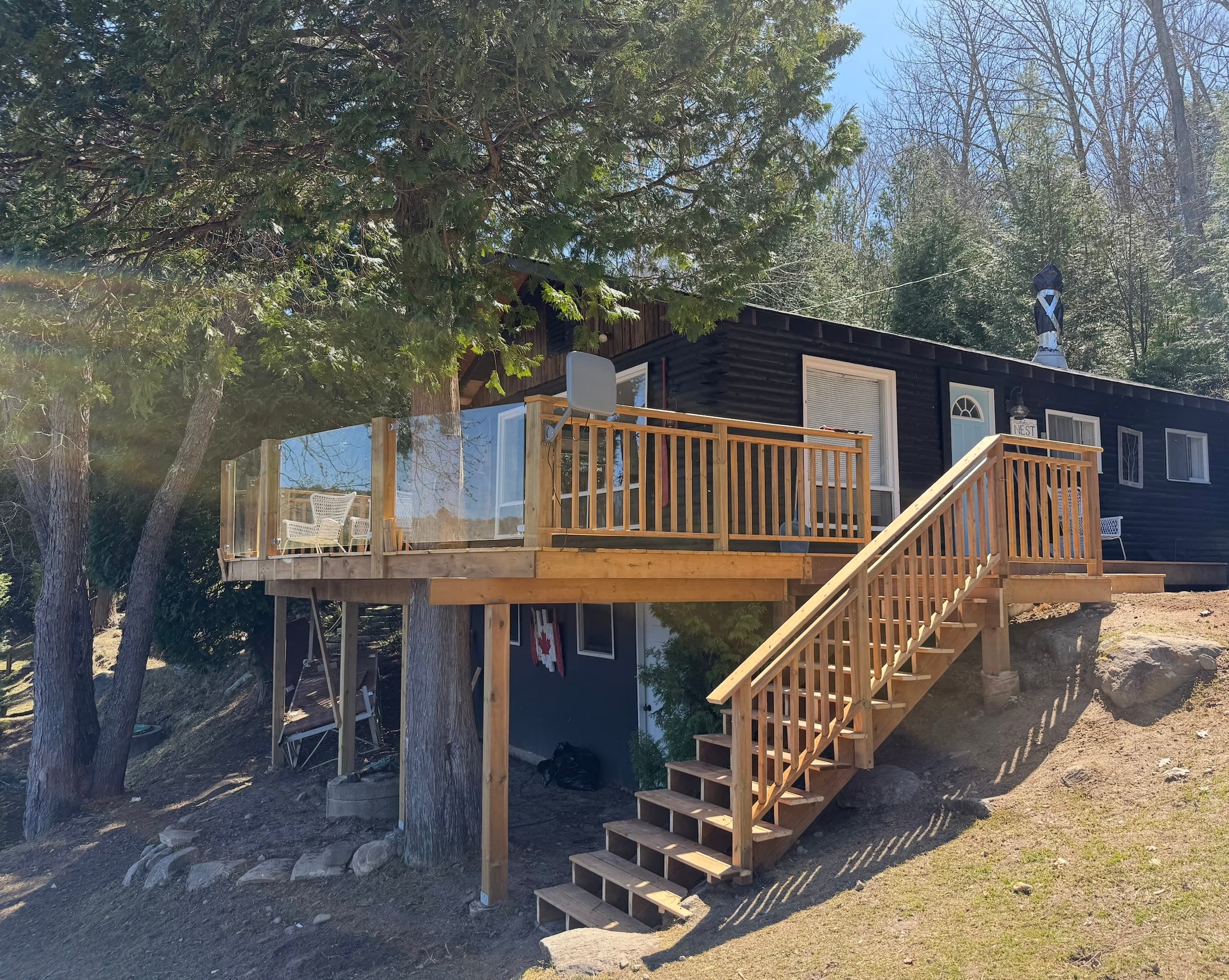 Exterior of the dark-clad cottage with raised glass-railed deck and wooden staircase.